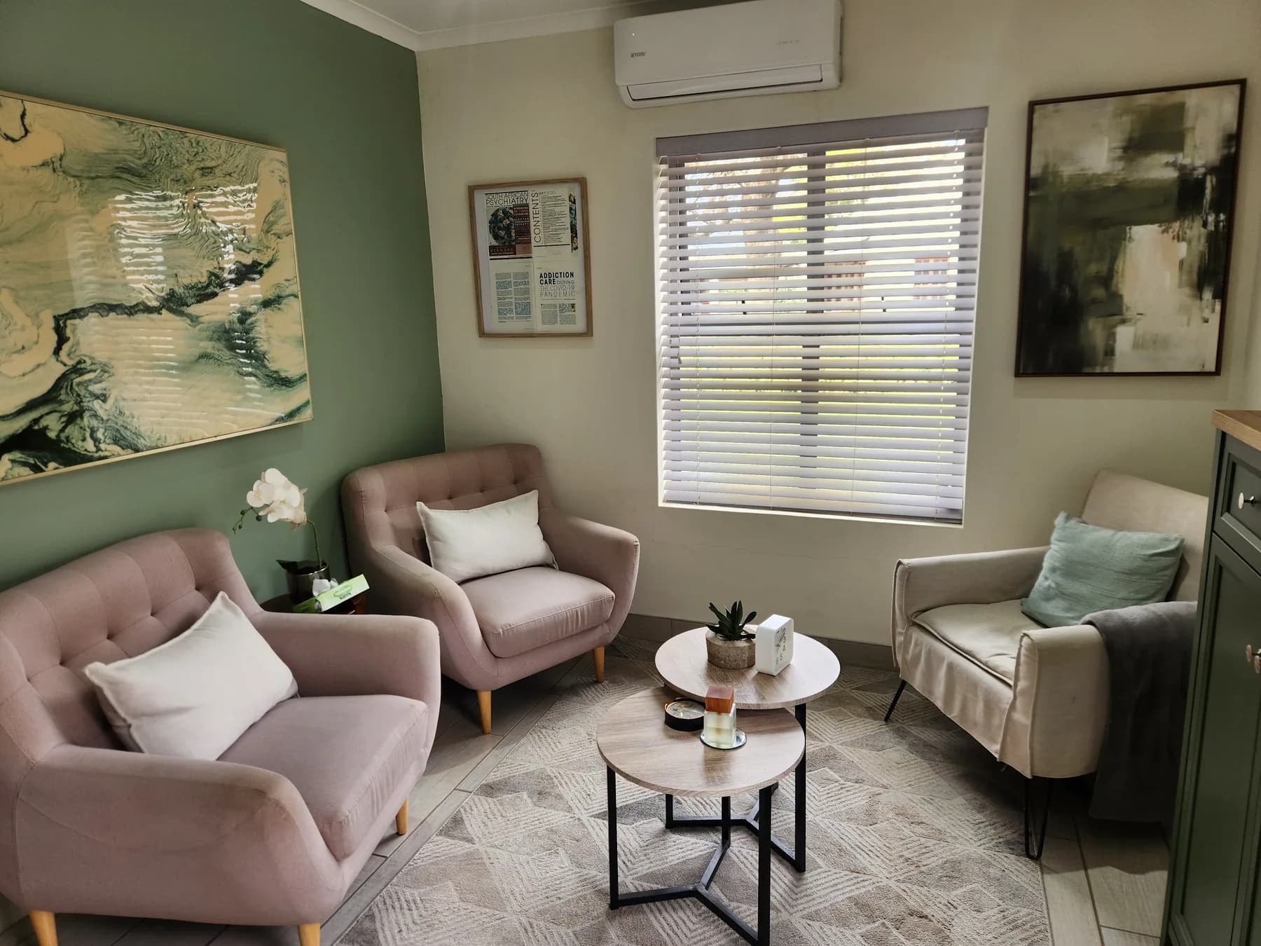 The Val de Vie consulting room: sage-green wall, dusty-pink armchairs and a low table.
